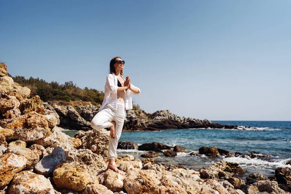 Mujer viajera disfruta de sus vacaciones en la costa del mar practicando yoga —  Fotos de Stock