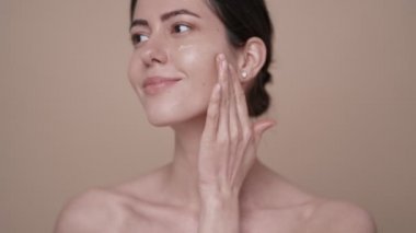 Genç bir kadın yüzüne krem sürüyor.