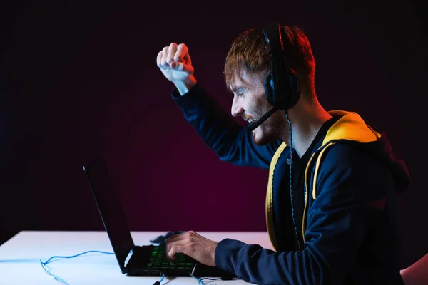 Guy jugador ganador con auriculares jugando videojuegos en su computadora personal —  Fotos de Stock