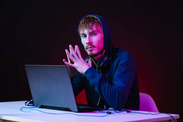 Profesionální hacker s notebookem sedět u stolu na tmavém pozadí — Stock fotografie