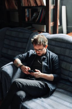 Kanepede oturan adam akıllı telefon kullanıyor.