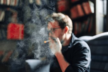 Arka planda kitaplarla Sigara İçen Adam portresi