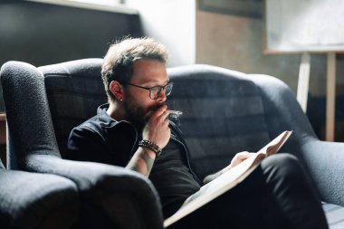 Yetişkin öğrenci üniversite kütüphanesinde sigara içerken kitap okuyor.