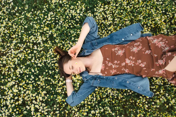 Ευτυχισμένη γυναίκα ξαπλωμένη σε ένα πράσινο χωράφι με χαμομήλι — Φωτογραφία Αρχείου