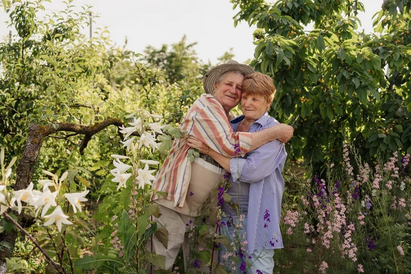 Gri ağaçlar ve çiçekler arasında kucaklaşan mutlu senatör çifti.