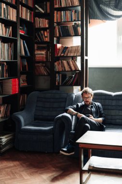 Kanepede oturan adam akıllı telefon kullanıyor.