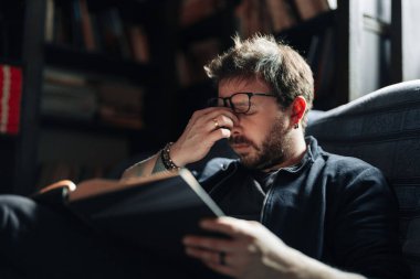 Üniversite kütüphanesinde kitap okuyan yorgun bir yetişkin öğrenci.