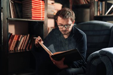 Yetişkin öğrenci üniversite kütüphanesinde sigara içerken kitap okuyor.