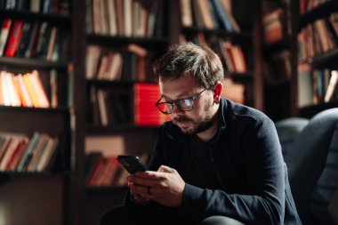 Kanepede oturan adam akıllı telefon kullanıyor.