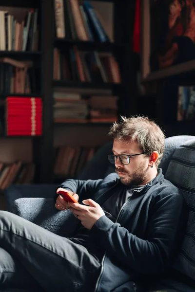 Uomo seduto su un divano con uno smartphone — Foto Stock