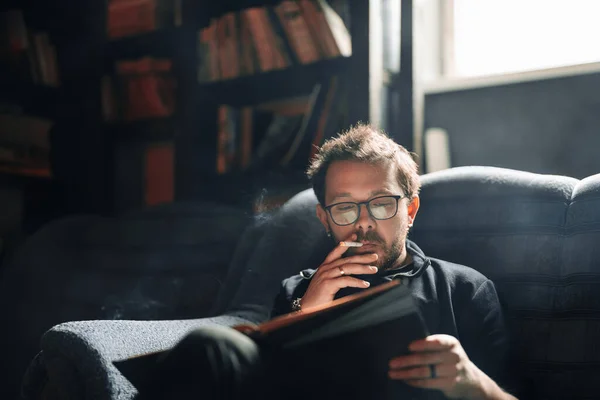 Studente adulto che legge un libro nella biblioteca del college mentre fuma — Foto Stock