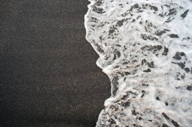 Kumlu bir sahilde yumuşak beyaz köpüklü bir dalga.