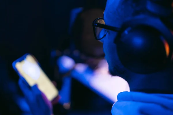 Mladý muž zpěvák v nahrávacím studiu vystupující v neonových světlech používat smartphone — Stock fotografie