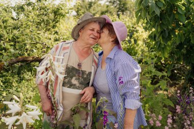 Sevimli yaşlı çift bahçede dinleniyor, ağaçlar ve çiçekler arasında sarılıp öpüşüyorlar. Mutlu bir hayat ve sağlıklı bir ilişki. Güzel aile.