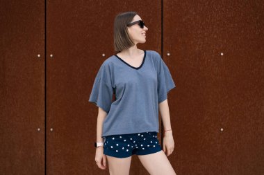 Young woman in casual t-shirt, shorts in sunglasses posing on rusty wall background. Urban style