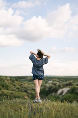 Carefree young woman daydreaming in nature with beautiful clouds in background
