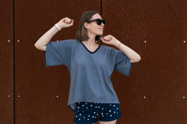 Young woman in casual t-shirt, shorts in sunglasses posing on rusty wall background. Urban style