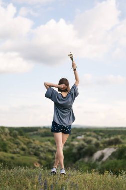 Carefree young woman daydreaming in nature with beautiful clouds in background