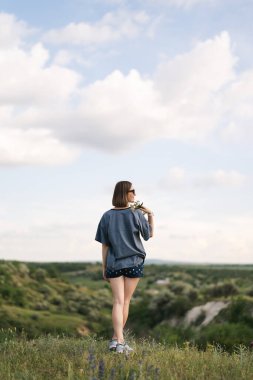 Carefree young woman daydreaming in nature with beautiful clouds in background