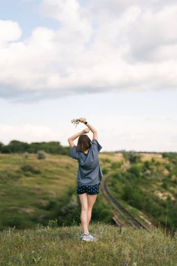Carefree young woman daydreaming in nature with beautiful clouds in background