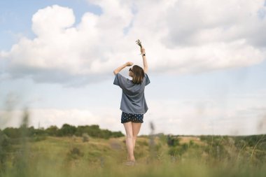 Carefree young woman daydreaming in nature touching beautiful clouds with finger