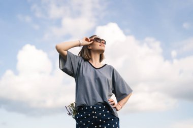 Carefree young woman daydreaming in nature with beautiful clouds in background