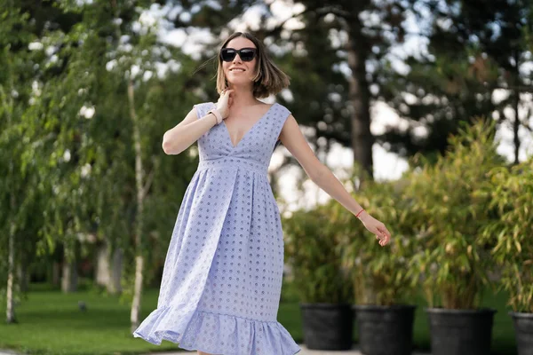 Cheerful caucasian woman in blue dress posing ourdoors in motion, on plants background