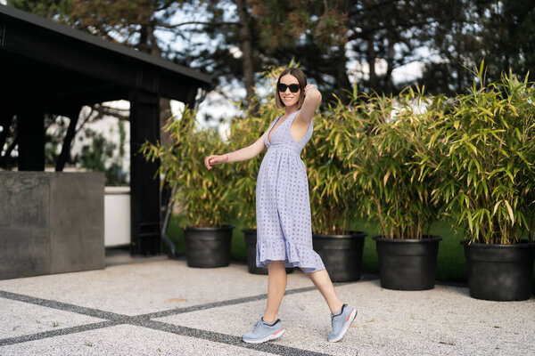 Веселая белая женщина в синем платье, позируя наши двери в движении, на фоне растений