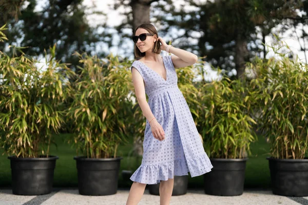 Cheerful caucasian woman in blue dress posing ourdoors in motion, on plants background
