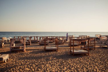View on empty sandy beach with wooden beach beds and blue clear water during calm morning. Mediterranean sea, Alanya, Turkey.