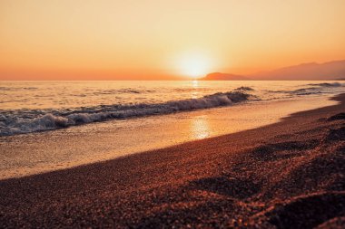 Beautiful abstract nature background with sea orange sunset on the coastline and splashing waves on the seashore