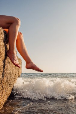 Young woman legs resting on a rock in the sea waves on vacation on the seaside
