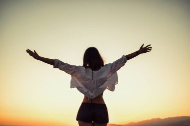 Cheerful young woman silhouette enjoying freedom holding arms open on sunset