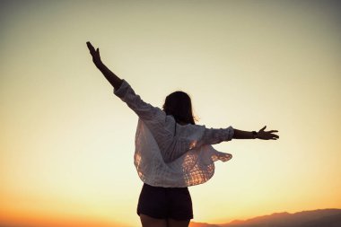 Cheerful young woman silhouette enjoying freedom holding arms open on sunset