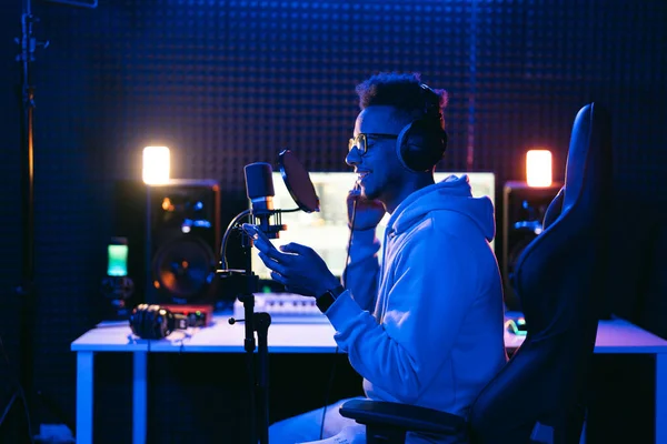 Erkek ses mühendisi, kıvırcık saçlı podcaster, kulaklık ses stüdyosunda akıllı telefon kullanarak yeni melodi ya da albüm kaydediyor..