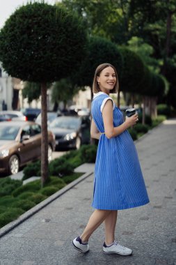 Mavi elbiseli güzel hamile bir kadın şehir sokaklarında yürüyor ve içki içiyor..