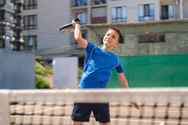 Açık alanda raketle padel oynayan genç bir delikanlı.