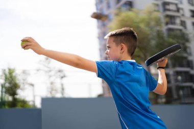 Açık alanda raketle padel oynayan genç bir delikanlı.