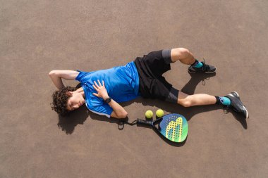 Açık hava kortunda elinde raket ve topla kıvırcık saçlı, sportif bir gencin portresi. Nokta konsepti, sağlıklı yaşam tarzı. Yere uzayı kopyala.