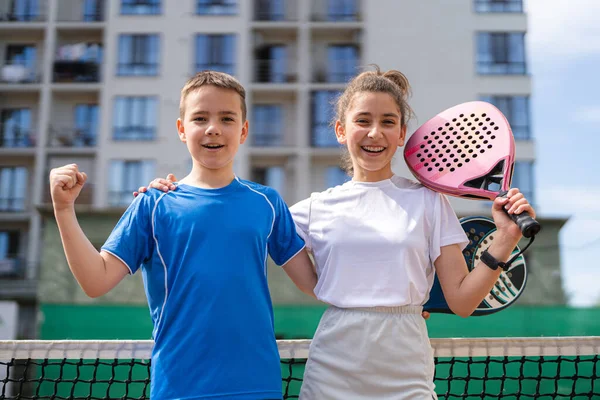 Çocuklar ve spor konsepti. Gülümseyen erkek ve kızın portresi dışarıda poz veriyor raketler ve tenis toplarıyla.