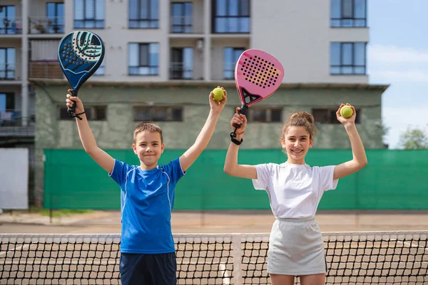 Çocuklar ve spor konsepti. Gülümseyen erkek ve kızın portresi dışarıda poz veriyor raketler ve tenis toplarıyla.