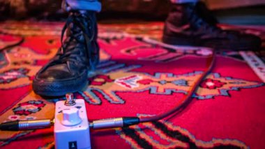 Siyah çizmeli erkek gitarist gitar sesini değiştirmek için pedal çeviriyor.