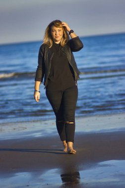 Genç sarışın kız bir sonbahar günü sahilde geziniyor..