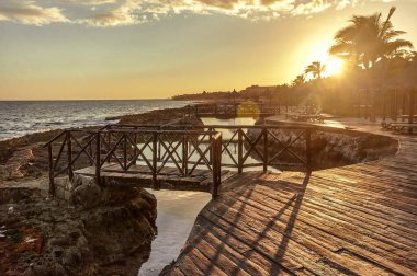 Gün batımında, Meksika 'da Puerto Aventuras sahilindeki kayaların arasında batan ahşap bir iskelede..
