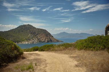 Sardunya 'nın güneyindeki doğal bir körfezde oluşturulan bir sahilde dağdan inen küçük toprak yol..