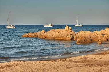 Mavi denizin ortasında Akdeniz 'deki bir uçurumun manzarası. Kayaların yakınındaki bazı lüks teknelerle birlikte..