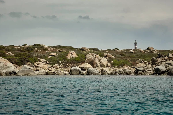 Lighthouse nestled in a natural promontory developed in horizontal liea under a dark and cloudy sky taken from in the middle of the sea.