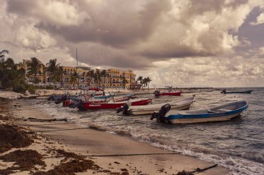 Playa del carmen, Mexico 20 august 2022: Several small fishing boats are moored by the sea in the beautiful beach of Playa del Carmen in Mexico with the background of the typical buildings of this place.