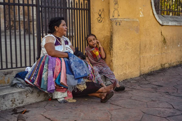 Valladolid, Mexico 20 august 2022: Old lady, a seller of handmade fabrics, sits in a corner of a sidewalk in the company of a child: Another example of what classism is in Mexico. Poor mexican people street side