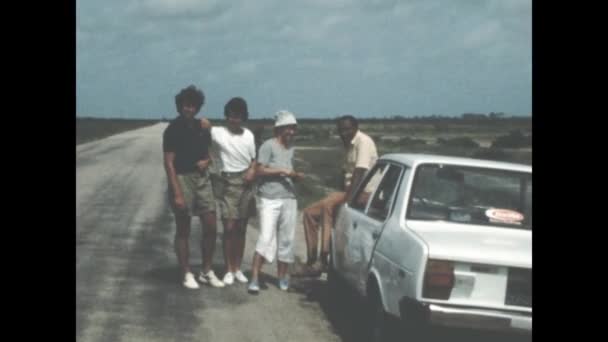 1971年 昭和46年 6月イタリア エルバ島 70年代の道路脇で壊れた車を持つ集団 友人は 道路旅行休暇の遠足で晴れた日に壊れた車を調べる 道路の旅の修復の内訳の若者のグループ — ストック動画